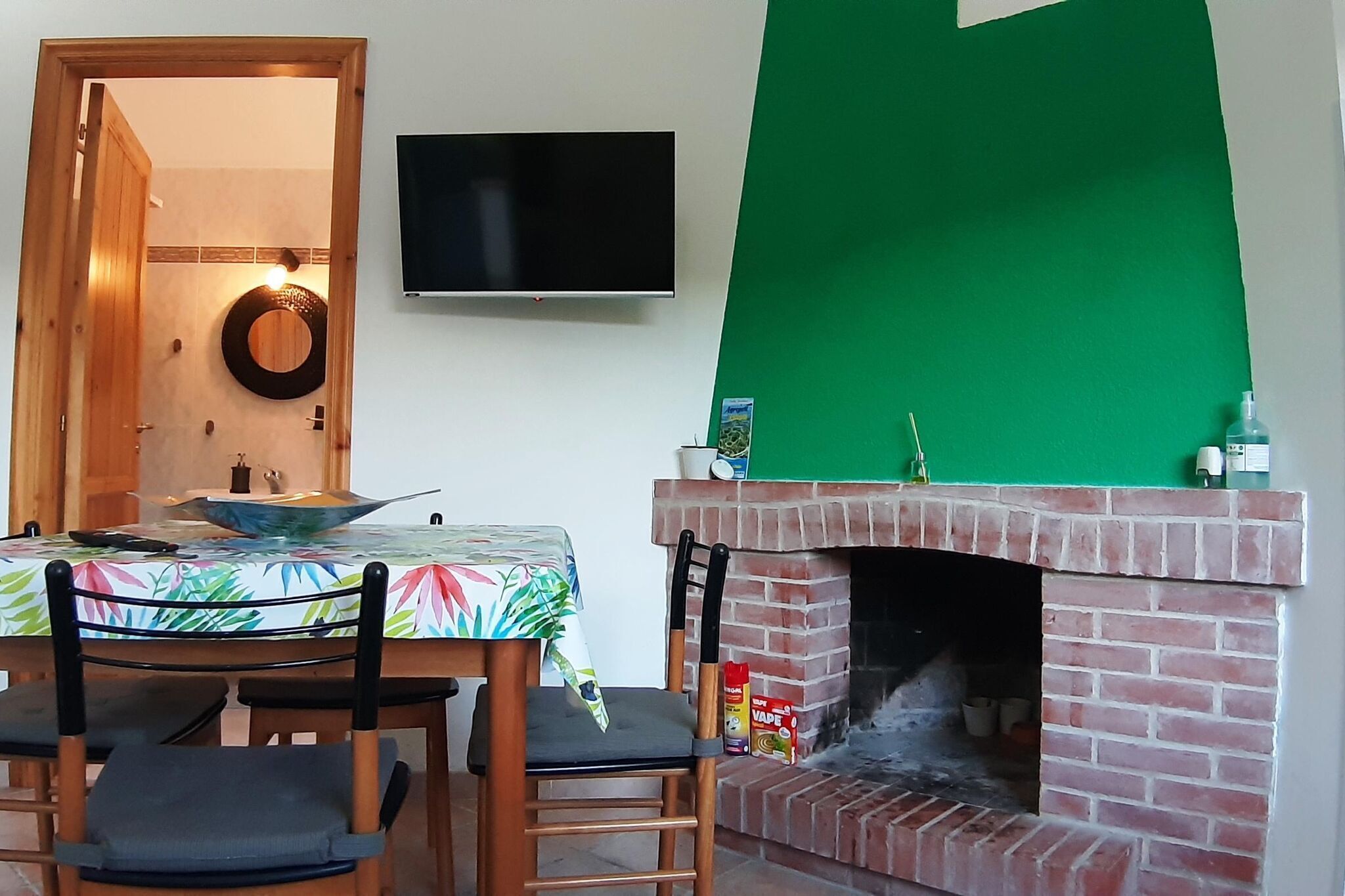 Un comedor con una mesa dispuesta para dos personas, una chimenea de ladrillo y un fondo verde.