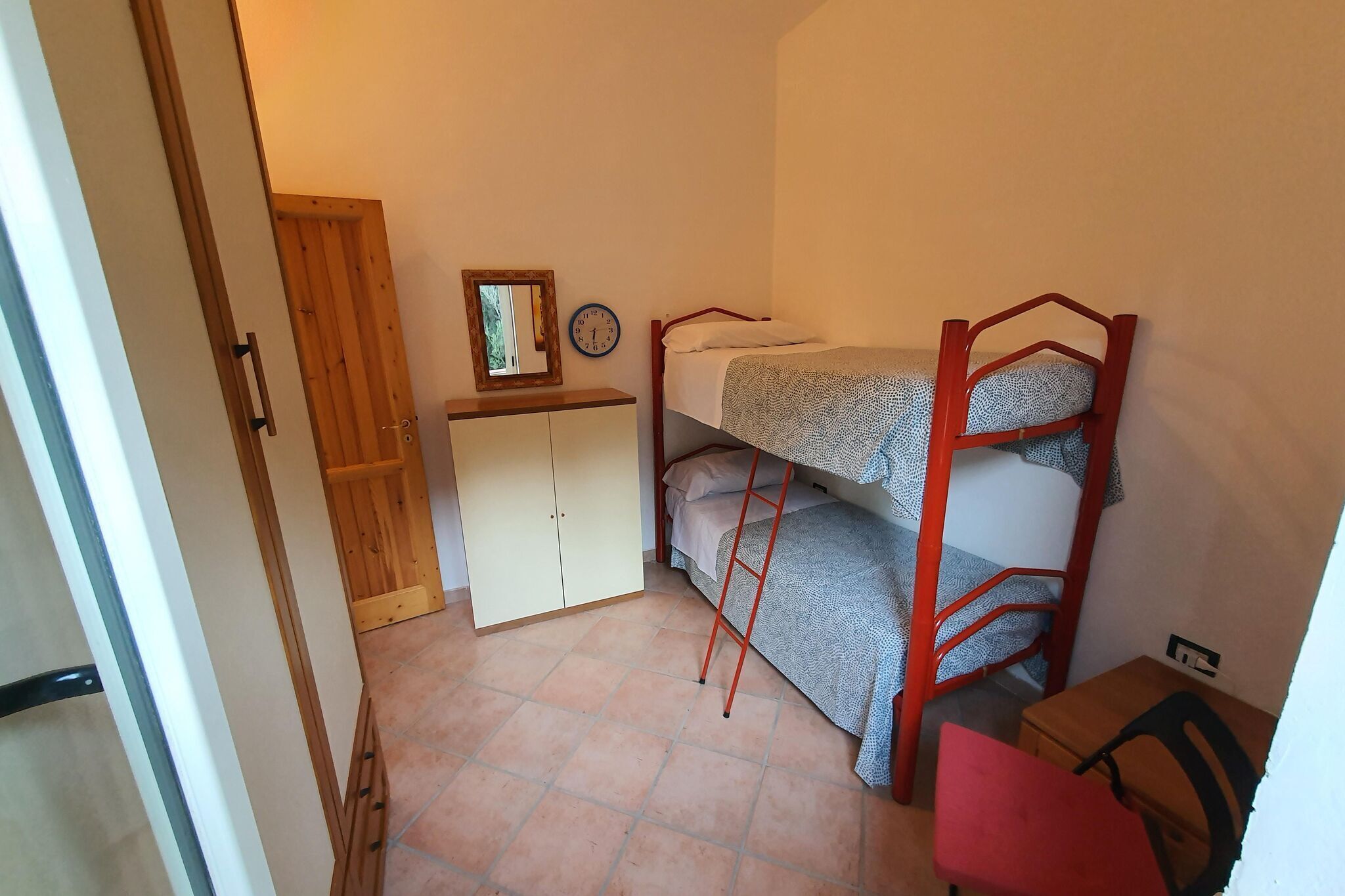 Ein kleiner, kompakter Raum mit Etagenbett, Holzschrank, Tisch und Stuhl.