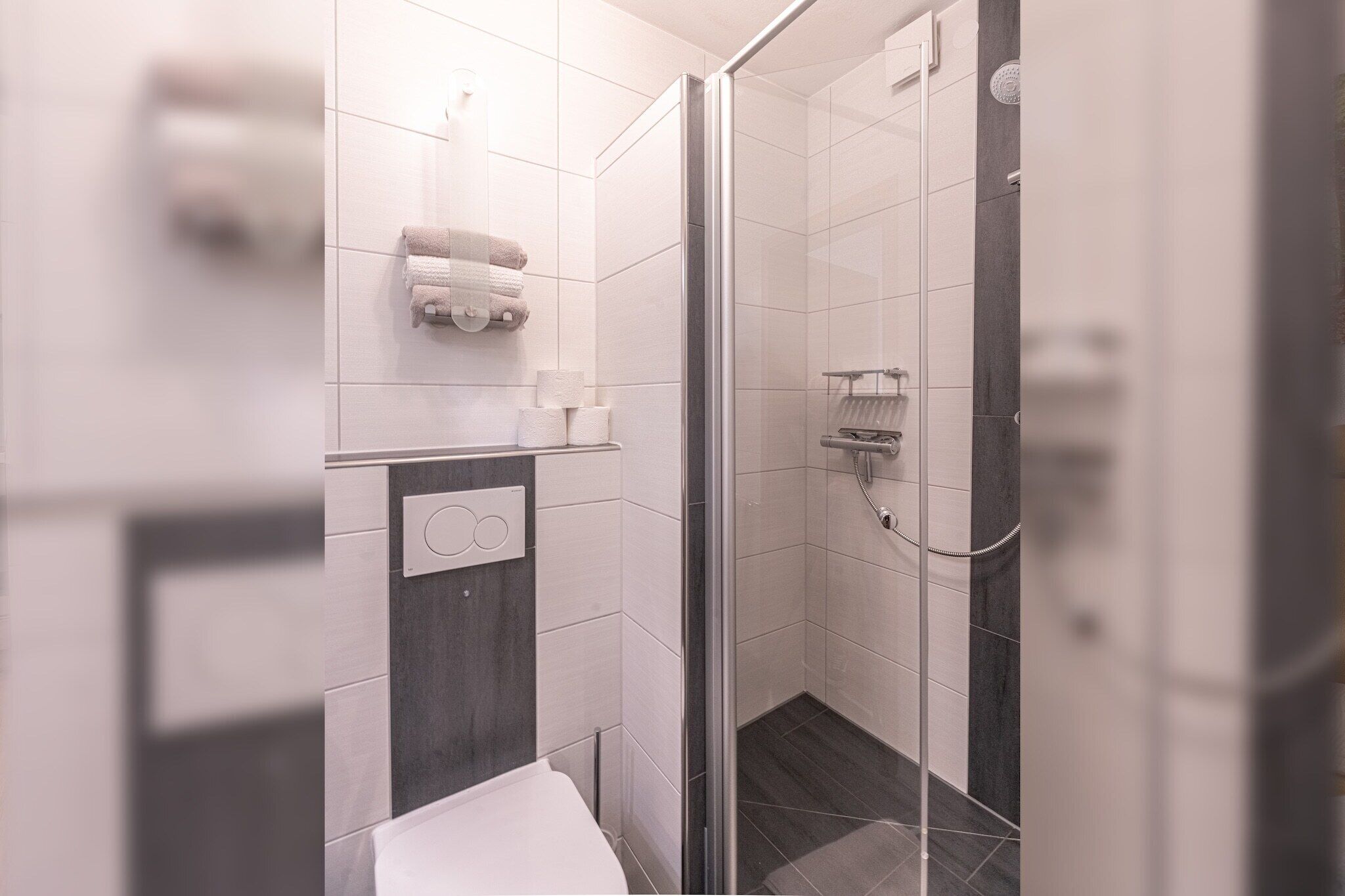 Ein modernes Badezimmer mit Duschkabine aus Glas, weißen Fliesen und Toilette.