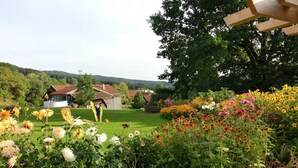 A garden with a variety of flowers, a wooden structure, and a house in the background. - Geraeumige Wohnung für 5 Personen in Drachselsried (Drachselsried)