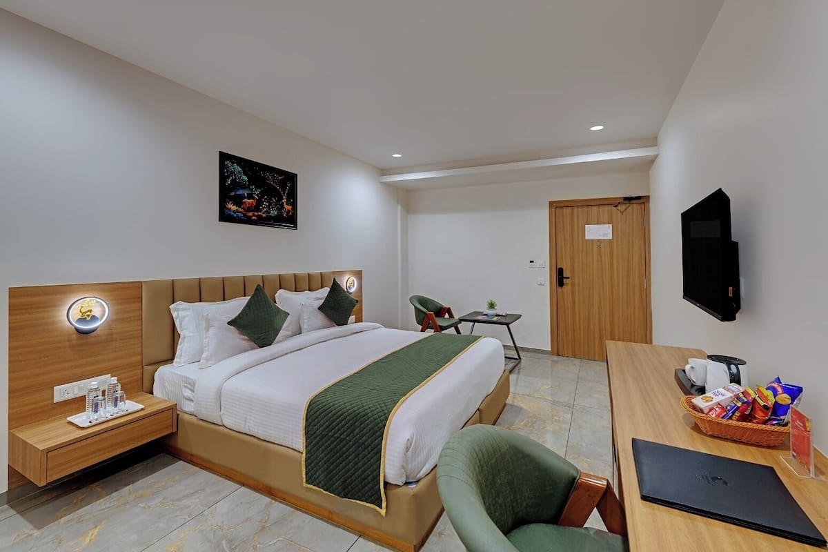 A modern hotel room with a bed, bedside table, chair, desk, and a TV.