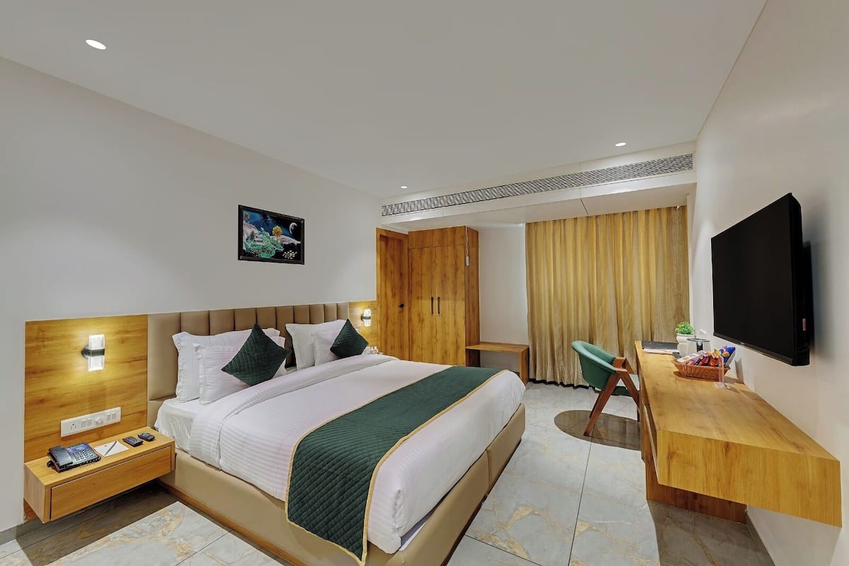 A hotel room with a bed, bedside table, desk, chair, TV, and a wardrobe.
