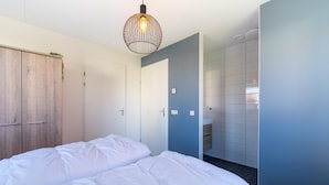 Een slaapkamer met een bed, een kledingkast, een hanglamp en een badkamer met een betegelde muur.