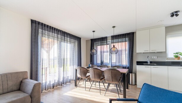 Een moderne woonkamer met een bank, een eettafel, stoelen en een keuken met kasten en een spoelbak.