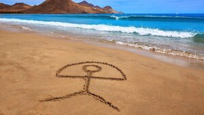 Una playa con un dibujo en la arena de una persona y montañas al fondo.