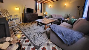 Een gezellige woonkamer met een bank, een houten salontafel, een schommelstoel en een televisie.