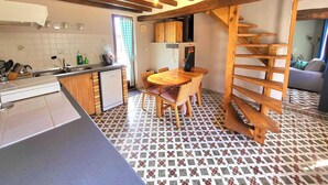 Een keuken met een betegelde vloer, houten balken in het plafond, een eettafel met stoelen en een trap.