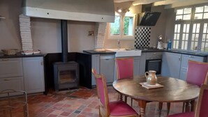 Een keuken met een houtkachel, een eettafel met stoelen en een geruit spatwand.