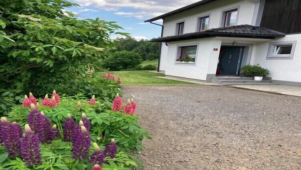 A modern two-story house with a gravel driveway and a garden with purple and red flowers.