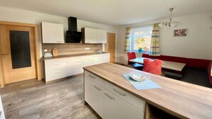 A modern kitchen with white cabinets, a wooden countertop, and a dining area with a red bench and table.