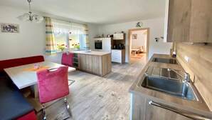 A compact kitchen with a central island, a dining area with red chairs, and a visible refrigerator.