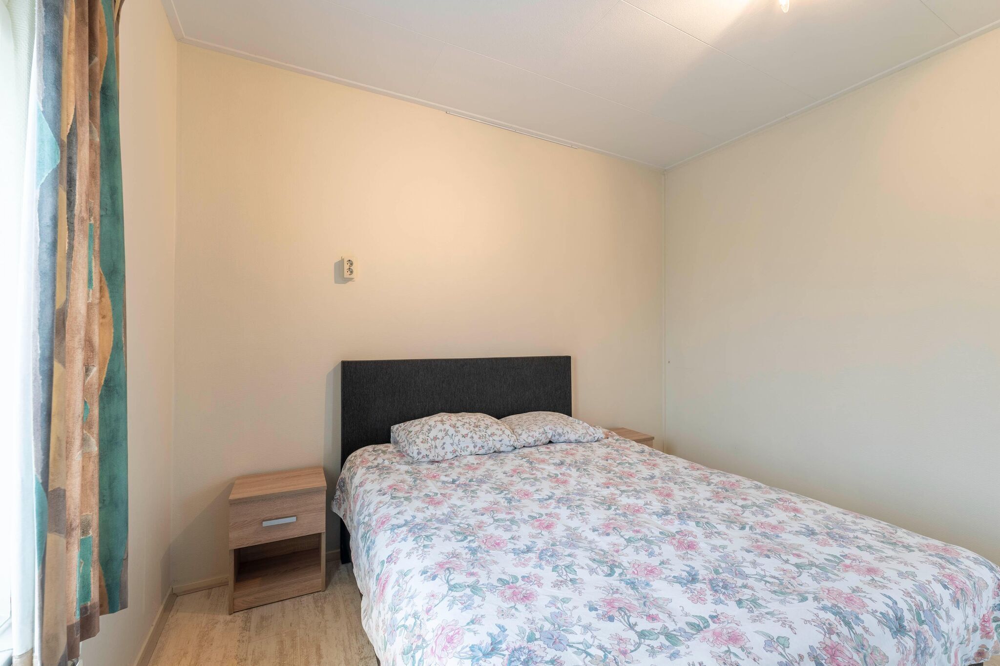 A bedroom with a bed, a nightstand, and a curtain.