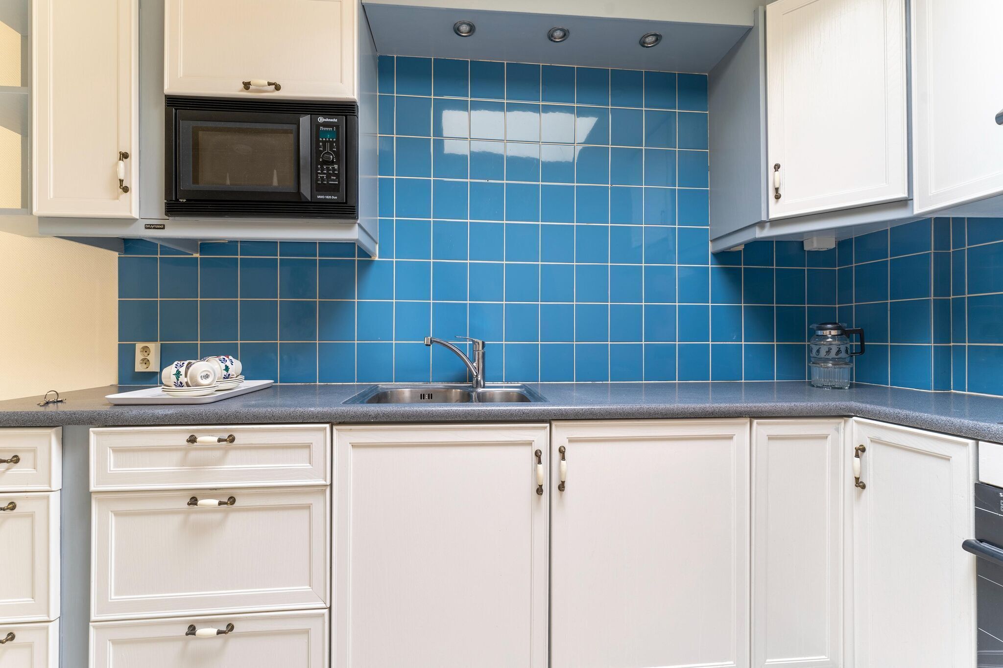 Eine Küche mit weißen Schränken, einer blauen Fliesenrückwand, einer Mikrowelle, einem Spülbecken und einem Geschirrgestell.