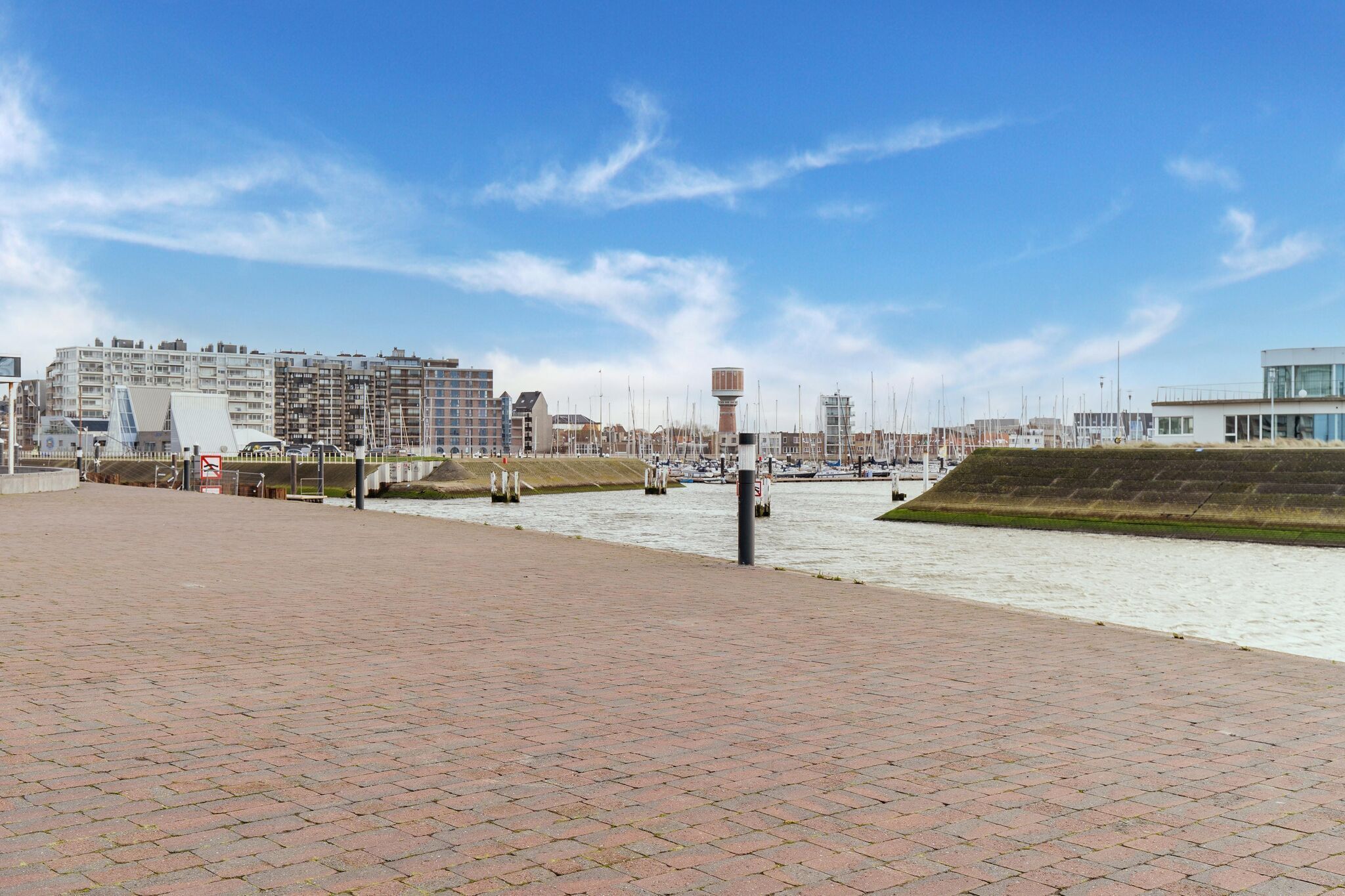 Une promenade en bord de mer, un ciel dégagé, un bâtiment moderne à la façade vitrée et une structure en forme de tour.