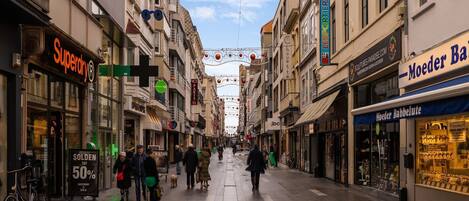 Een voetgangersstraat vol winkels en restaurants, waaronder een zichtbare Superdry-winkel en een Moeder Babbelute winkel.