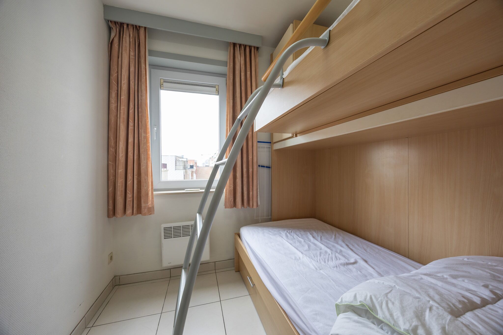 A bunk bed room with a window, curtains, and a ladder.