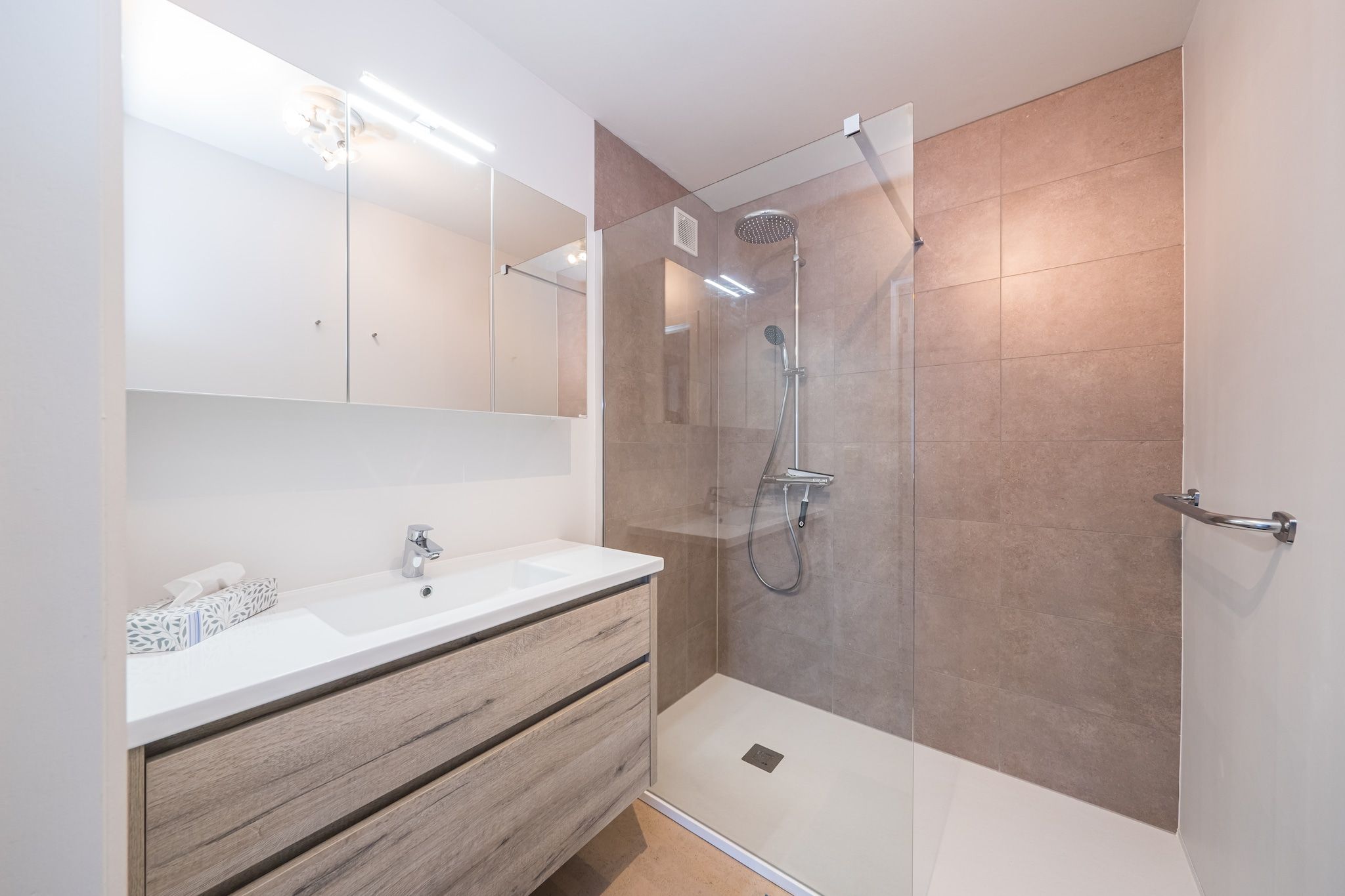 A modern bathroom with a glass-enclosed shower, a wooden vanity, and a large mirror.