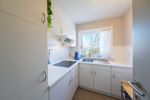 Et lille køkken med hvide skabe, indbygget mikroovn, elkedel og et vindue med udsigt.