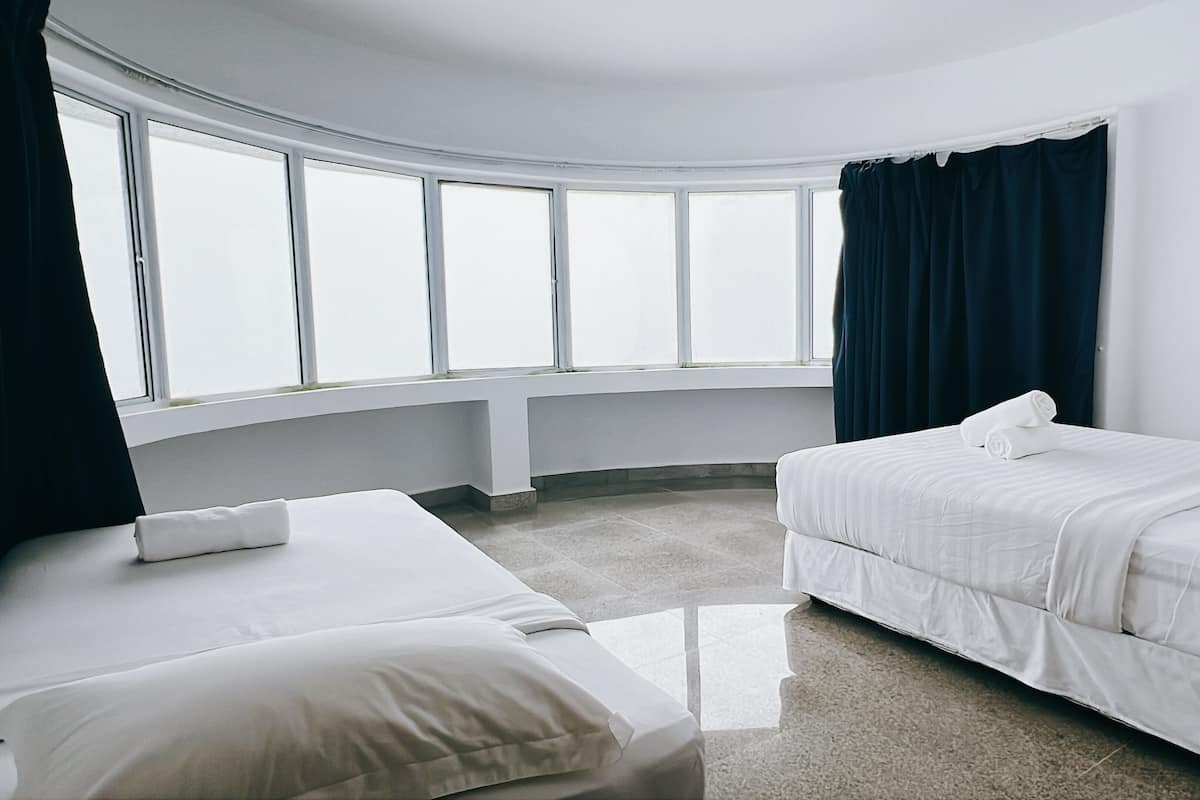 Una habitación de hotel con dos camas, un ventanal grande y una cortina oscura.