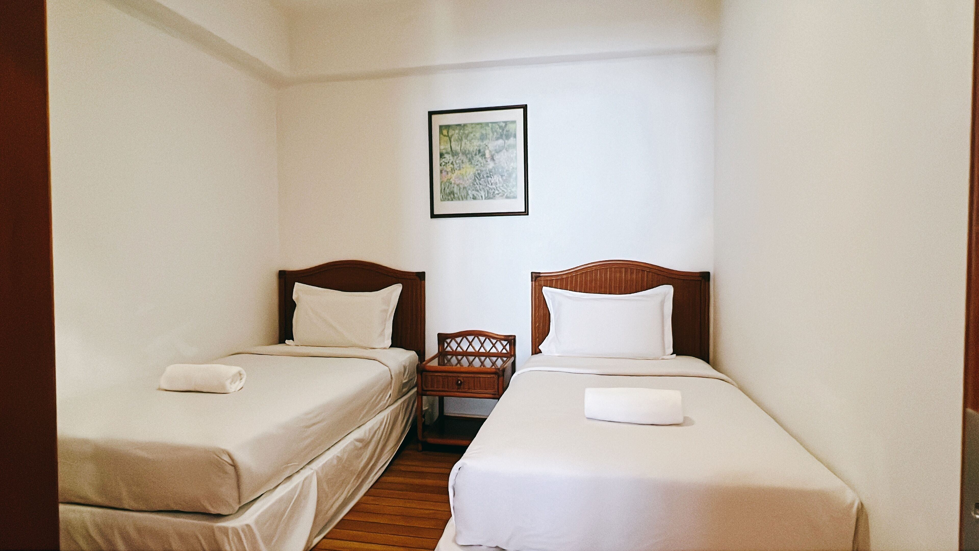 A hotel room with two single beds, each with a wooden headboard and white bedding.