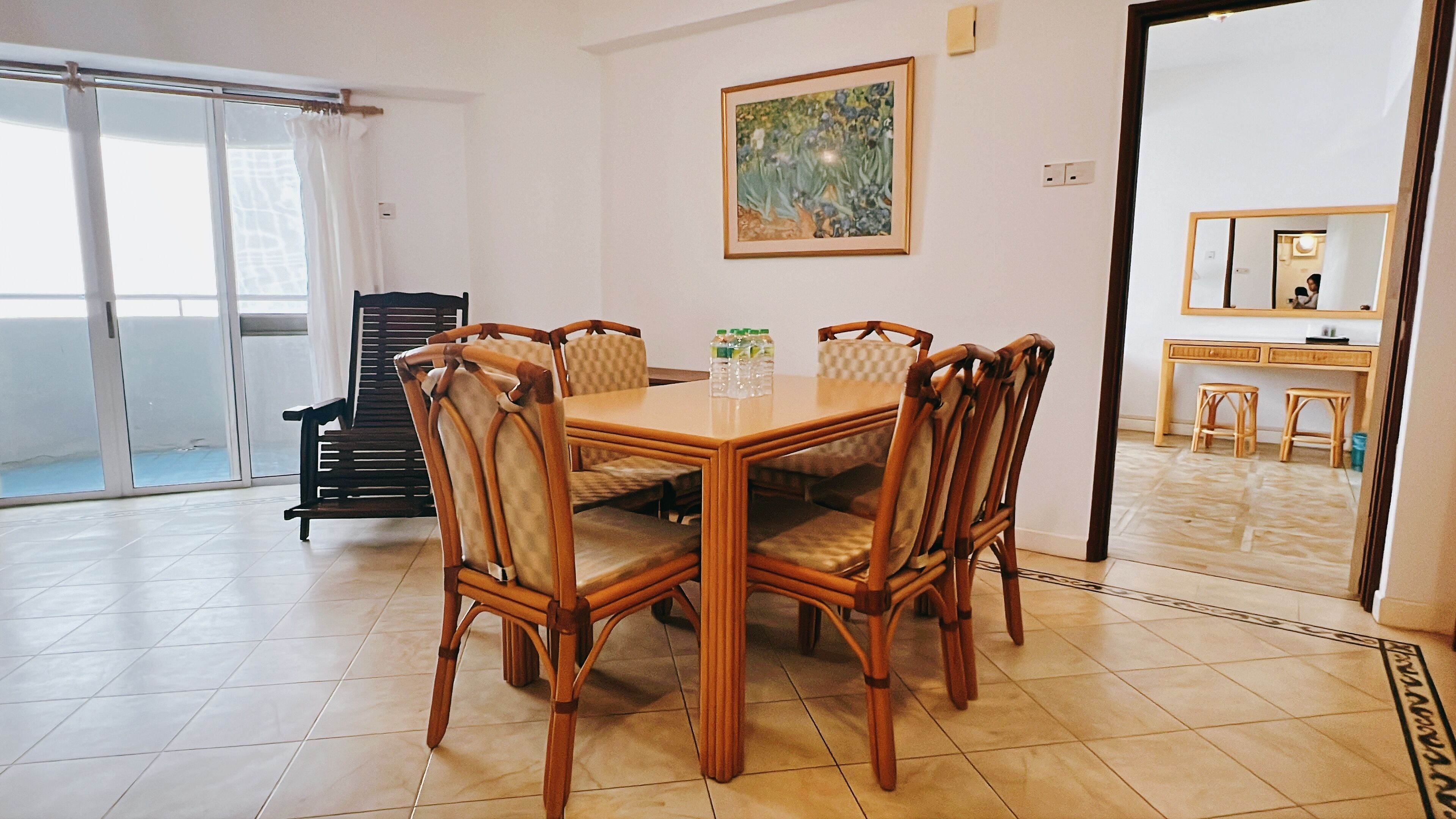 A dining area with a wooden table and chairs, a painting on the wall, and a view of the outside through a sliding door.