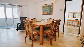 A dining area with a wooden table and chairs, a painting on the wall, and a view of the outside through a sliding door.