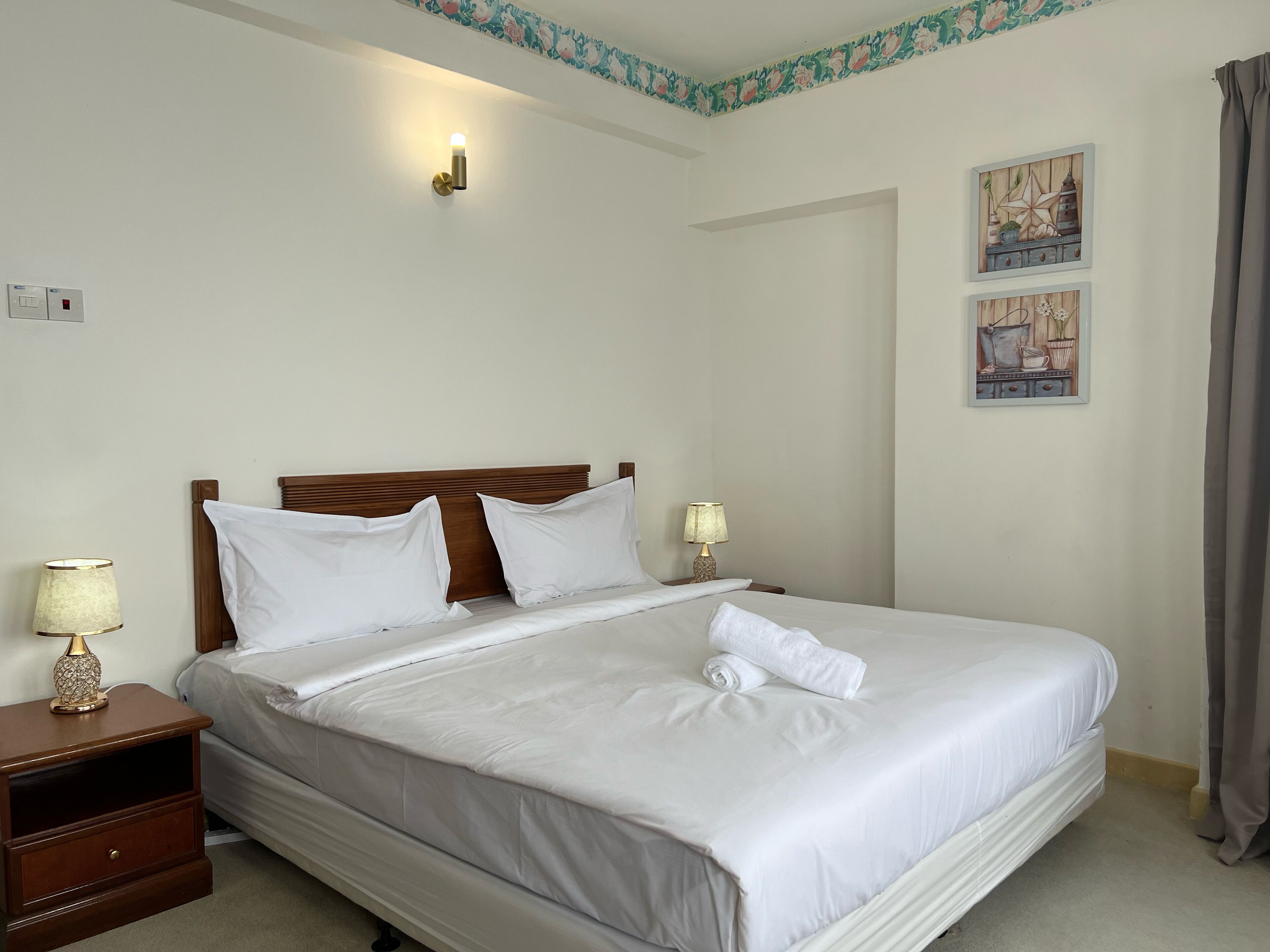 A neatly made bed with white linens, a wooden headboard, and two bedside lamps.