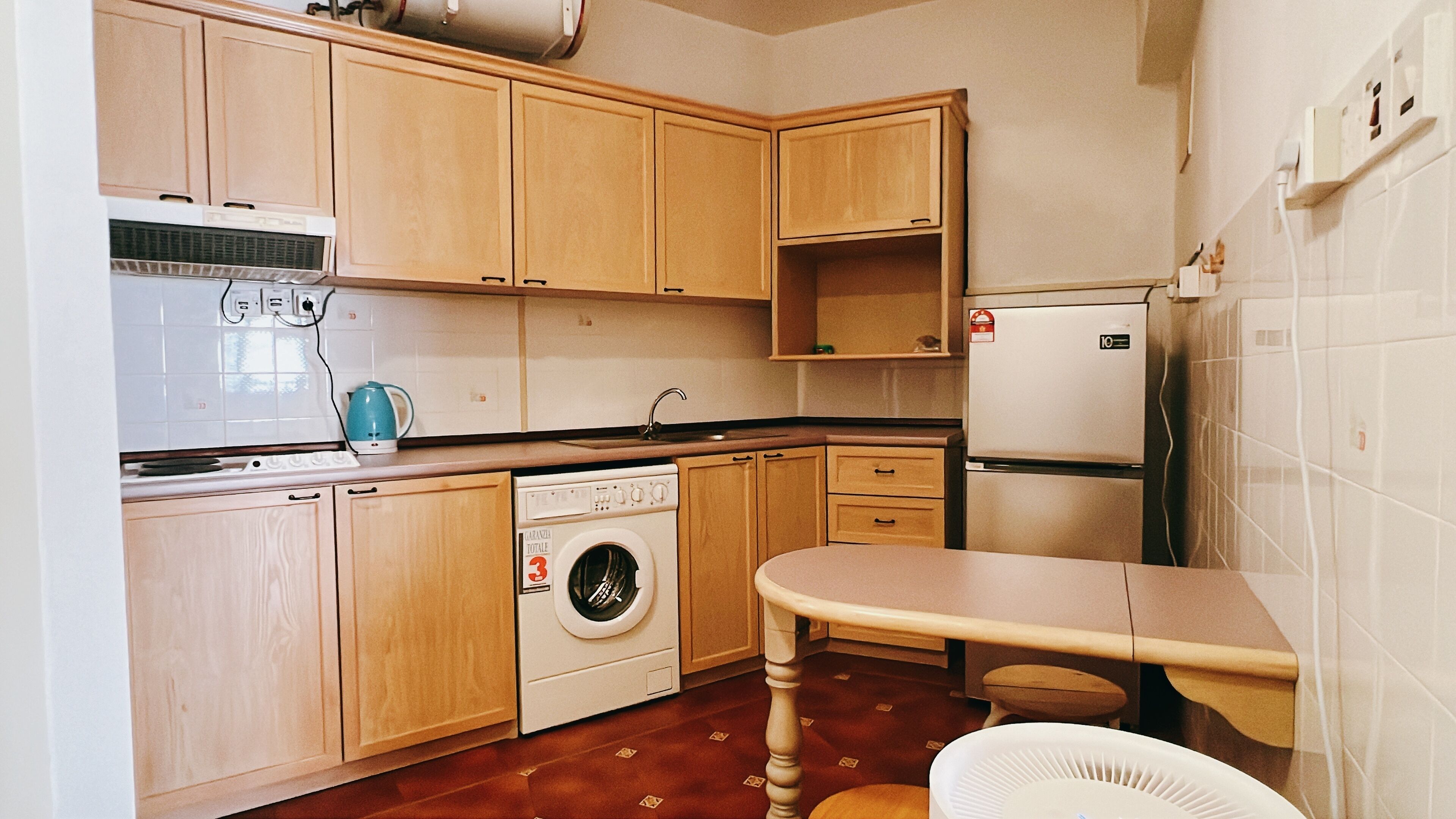 A compact kitchen with wooden cabinets, a washing machine, a refrigerator, and a sink.
