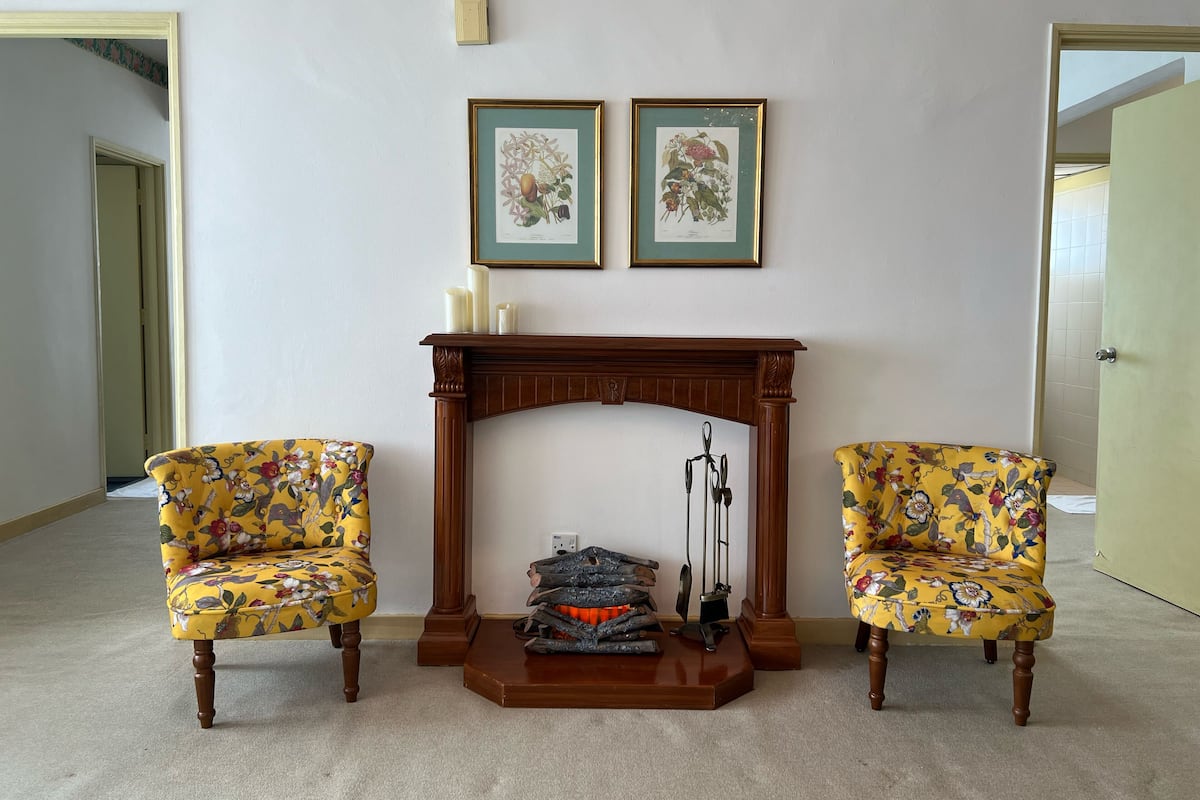 Una habitación con chimenea, dos sillones y dos láminas botánicas enmarcadas en la pared.