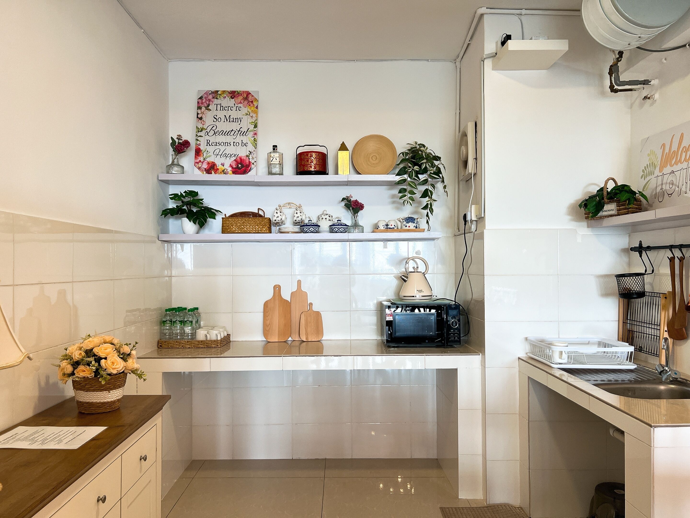 A kitchen with white tiles, wooden countertops, and shelves with kitchenware and decorative items.