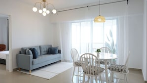 A modern living room with a light blue sofa, white chairs, a round dining table, and a large window with sheer curtains. - Cloud Forest Homestay Genting Highlands (Genting Highlands)