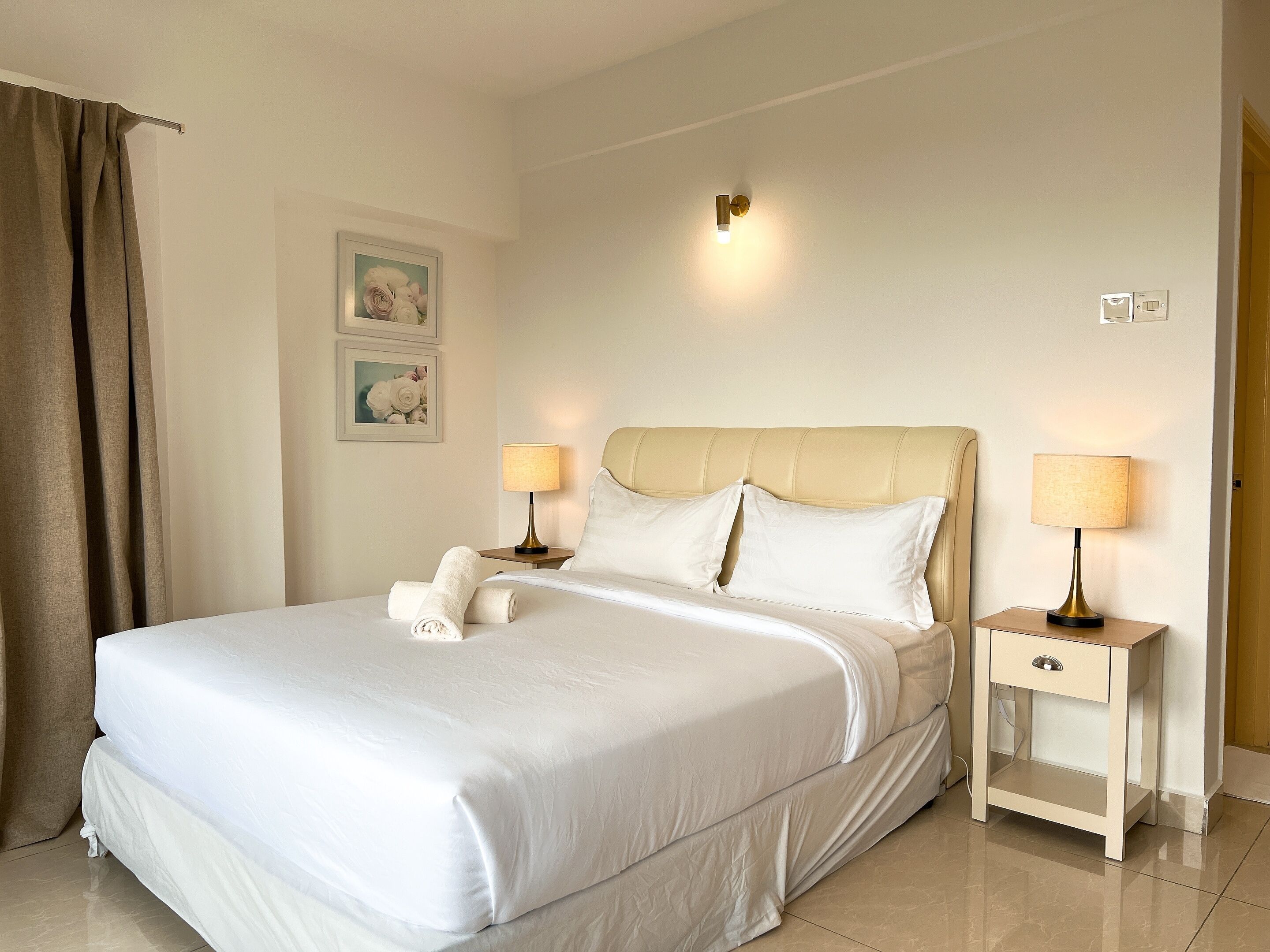 Uma cama bem arrumada com roupa de cama branca, duas mesas de cabeceira com abajures e um ponto de luz fixado na parede.