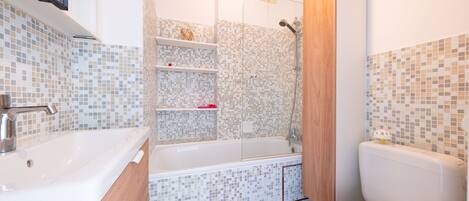 A bathroom with a white sink, a bathtub, and a toilet. There are shelves with toiletries and a shower area.