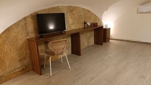 A room with a TV mounted on a wooden shelf, a wicker chair, and a small table with decorative items. - Naples historic center cozy little house centrally located equipped with every comfort (Napoli)
