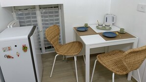 A compact kitchenette with a white refrigerator, a small table with two chairs, and a window with a striped curtain. - Naples historic center cozy little house centrally located equipped with every comfort (Napoli)