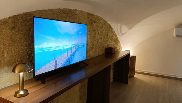 A television on a wooden stand against a textured wall, with a wooden floor and a lamp beside it. - Naples historic center cozy little house centrally located equipped with every comfort (Napoli)