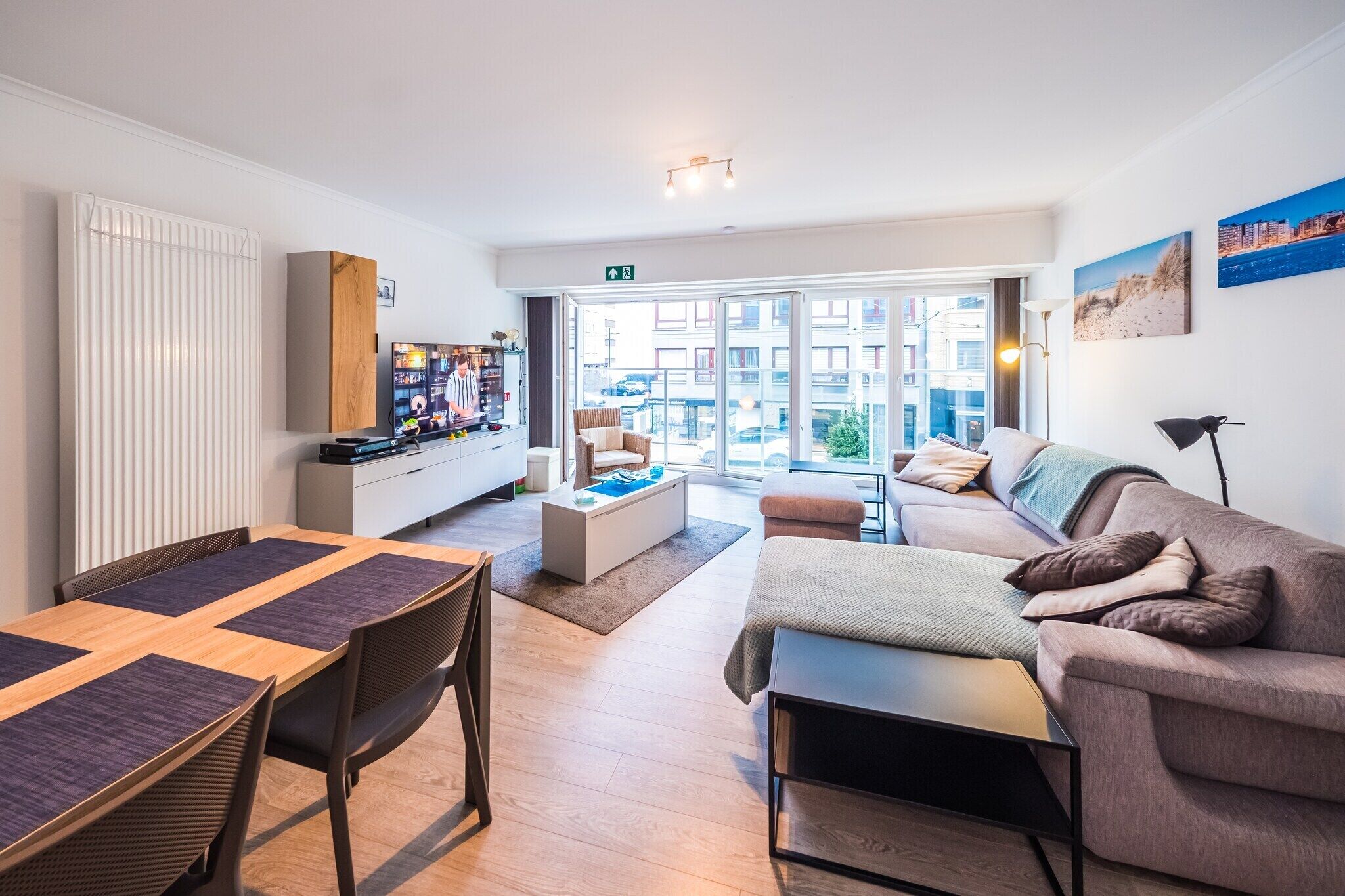 A modern living room with a sofa, coffee table, and a dining area with a table and chairs. There is a large window providing a view of the city.