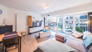 Una sala de estar moderna con una mesa de comedor de madera, un sofá, un televisor y un ventanal con vista a la ciudad.
