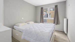 A bedroom with a bed, a window with curtains, a radiator, and a view of a building outside. - Pleasant apartment on the 2nd floor (Blankenberge)