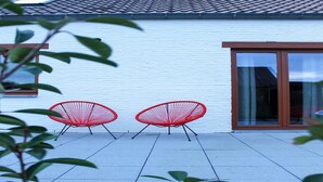 A white building with a tiled roof and a glass door. There are two red chairs outside.