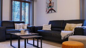 A modern living room with a dark leather sofa, a wooden coffee table, and a small orange ottoman.
