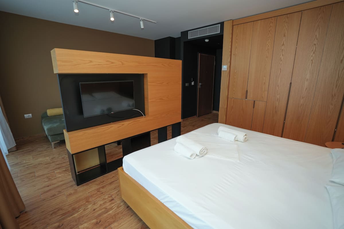 Un dormitorio moderno con cabecera de madera, televisor de pantalla plana, cama con ropa blanca y un armario.