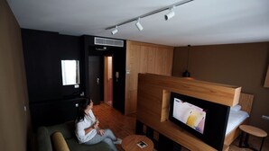 En moderne stue med sofa, tv ophængt på et træstel, et lille rundt bord og en fjernbetjening på sofaen.