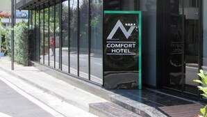 En moderne hotelindgang med en glasfacade, et skilt for Comfort Hotel, og frit udsyn til gaden.