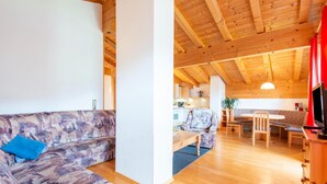 A living room with a sofa, a dining area with a table and chairs, and a kitchen in the background. - Chalet in Gattererberg near Ski Slopes (Stummerberg)