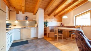 A kitchen with wooden beams, a dining area with a table and chairs, and a window with curtains. - Chalet in Gattererberg near Ski Slopes (Stummerberg)