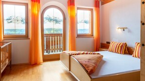 A bedroom with a wooden bed, two windows with curtains, a view of the outdoors, and a small balcony. - Chalet in Gattererberg near Ski Slopes (Stummerberg)