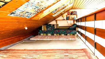 Ein gemütliches Schlafzimmer im Dachgeschoss mit schrägen Wänden, einem gemusterten Teppich, einem farbenfrohen Sofa und einem Bücherregal.