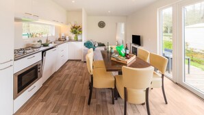 A modern kitchen with white cabinets, a built-in oven, and a dining area with a wooden table and beige chairs.