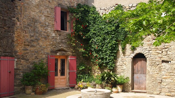 Un patio con una fuente de piedra, contraventanas rojas y un muro de piedra.